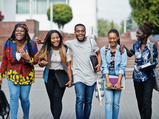Group of five african college students spending time together on campus at university yard. Black afro friends studying. Education theme.